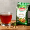 Amazon Plus Tea Premix 1kg price shown with a glass of brewed tea and spices on wooden surface
