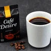 Cafe Desire coffee premix bulk packs beside a white cup of black coffee and coffee beans