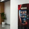 Nescafe vending machine in office lobby near plant and white wall