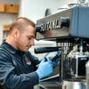 Technician repairing black DeLonghi coffee machine for coffee machine repair service Mizoram in office setting