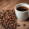 White ceramic cup of coffee next to roasted beans on wooden table for Atlantis Coffee Machine near me