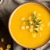Close-up of a bowl of creamy pumpkin soup garnished with herbs and diced vegetables