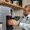 Man using a silver ATLANTIS COFFEE MACHINE, compact model, black accents, suitable for office use