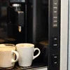 Black coffee vending machine dispensing coffee with two white cups and dairy whitener for coffee vending machines nearby