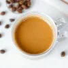 White cup of instant coffee premix for office with coffee beans scattered on wooden surface