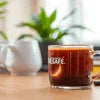 Nescafe branded clear glass cup with coffee on wooden table, ideal for coffee machine rental in office settings