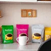 Amazon Plus instant coffee premix f with pink, purple, yellow, and white packaging displayed with a white coffee cup for office use