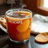 Nescafe coffee in clear glass cup with slice of dried orange on wooden table near window, coffee machine grugram use