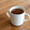 White ceramic cup filled with coffee on wooden table near coffee machine grugram