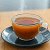 Clear glass cup of tea on black saucer showcasing instant tea premix for office use by instant tea premix suppliers in Gurgaon