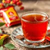 Clear glass cup with brown Amazon Plus tea premix suppliers in Noida served on a clear saucer with colorful packets in background
