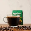 Amazon Plus coffee premix India pack with black coffee in clear cup and coffee beans on table