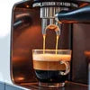Close-up of a black DeLonghi coffee machine brewing espresso into a small glass in an office setting, best coffee machine in Hisar